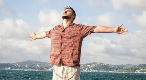 Uomo con le braccia aperte sulla spiaggia mentre respira profondamente davanti al mare.