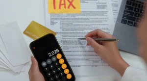 Person calculating figures on tax documents with a calculator and pen