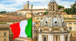 Bandiera italiana che sventola in primo piano con Roma sfocata sullo sfondo