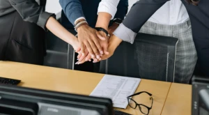 Several hands joined in the center symbolizing cooperation in an official mission or institutional collaboration