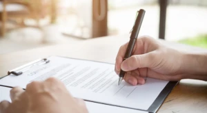 Persona escribiendo documentos oficiales en un registro, representando la transcripción de actos del estado civil para ciudadanos italianos residentes en el extranjero