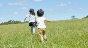 Dos niños corren alegremente por un campo verde bajo la luz del sol, simbolizando libertad y futuro