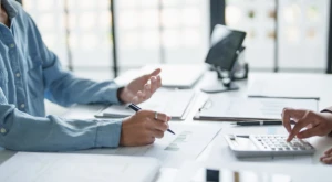 Profesionales sentados en un escritorio con documentos, ordenador portátil y materiales de estudio, revisando trámites relacionados con la contratación de trabajadores extranjeros y la Tarjeta Azul UE.