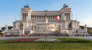 Fachada del Parlamento italiano en Roma, con su arquitectura histórica iluminada y personas caminando frente al edificio